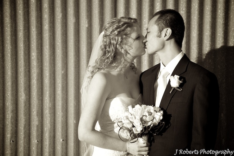 Sepia kissing couple with corrugated iron wall behind - wedding photogrpahy sydney